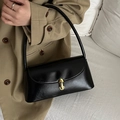 Glossy black baguette bag with gold metal clasp carried on shoulder by model - Black