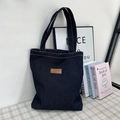 Borsa tote in denim blu scuro con toppa in pelle vintage su scrivania minimalista - Stile Uno Blu Profondo