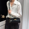 Chic black shiny leather crossbody bag with gold hardware shown on a model - Black
