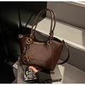 Gros plan du sac cabas en cuir marron foncé brillant avec relief et breloques de mode - Café avec Pendentif