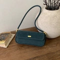 Detalle de bolso baguette de ante verde oscuro con elegante hebilla dorada sobre madera - Verde Turquesa