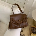 Borsa tote in pelle marrone vintage con chiusura dorata su un divano bianco - Marrone