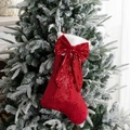 Red sequin Christmas stocking with a large bow and white plush trim hanging on a tree - Red