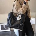 Retro black leather tote bag with white dog charm shown on a shoulder by a female model - Black With Rabbit Pendant