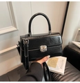Detail einer glänzenden schwarzen Handtasche mit Silberschnalle, in der Hand gehalten - Schwarz