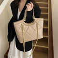 Beige quilted leather tote bag with gold chain strap held by a model in a suit - Khaki
