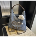 Detail view of washed grey canvas tote bag with brown leather accents and plush charm - With Charm / Denim Blue