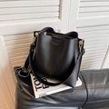 Bolso saco negro elegante con correa ancha y detalles dorados sobre un libro - Negro