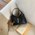 Close-up of black leather pleated bag with silver lock and horse charm on a white sofa - Black