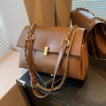 Braune Leder-Tote-Tasche mit goldener Kette und Metallschloss in warmer Innenumgebung - Braun