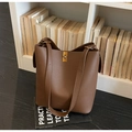 Détail d'un sac seau en cuir marron grainé avec fermoir doré et logo embossé chic - café