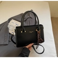 Gros plan d'un sac à main noir avec logo doré, poignées et pendentif en forme de cœur - Noir avec pendentif