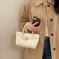 Schicke cremefarbene Lederhandtasche mit Zierschnalle, getragen von einem Modell im Trenchcoat - Cremeweiß