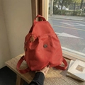 Mochila compacta de nailon rojo con logo metálico en un taburete de madera - Rojo