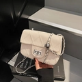 Beige tweed quilted chain bag with silver turn-lock clasp on minimalist book background - White