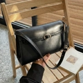 Sac bandoulière carré en cuir noir minimaliste avec boucle dorée sur une chaise - Noir