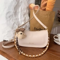 Cream-colored crescent baguette bag with gold chain and plush puppy charm detail - Milk White