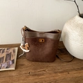 Detailed macro view of dark brown suede bucket bag with gold twist lock and wooden horse charm - Brown