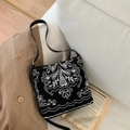 Détail d'un sac seau noir avec broderie blanche vintage sur un trench-coat et livre - Noir