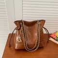 Quilted brown bucket bag with gold chain strap and D-charm on wooden table - Tan
