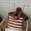 Détail d'un sac cabas rayé en maille pelucheuse avec des franges marron et crème sur une chaise - Marron
