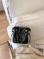 Quilted black bucket bag with gold chain strap and PAN'TOR LONDON logo on white sofa - Black