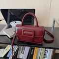 Detailed view of deep red square handbag with metal buckle on a minimalist bookshelf - With Charm / Red