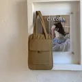 Detail of coffee quilted tote bag with vertical stitching and front flap pocket on white wall - Khaki