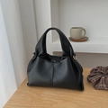Elegant black lychee grain cloud handbag with gold hardware rings on a wooden table - Black