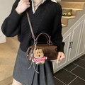 Brown faux leather pillow bag with buckle and teddy bear charm on model in stairs - Single Bag + Charm / Coffee