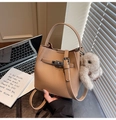 Detailed shot of caramel lychee leather bucket bag with silver metal lock and plush bunny - Khaki With Pendant