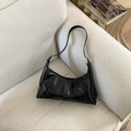 Detalle de bolso baguette negro brillante plisado con anillos de plata sobre un sofá - Negro