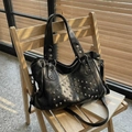 Bolso tote negro con remaches plateados y correa ajustable sobre una silla de madera - Negro