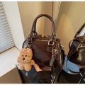 Detail of glossy brown Boston bag featuring golden hardware and plush dog pendant charm - With Charm / Coffee
