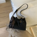 Black matte suede bucket bag with leather buckle and elephant tassel charm on a sofa - Black