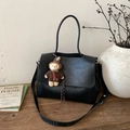 Dettaglio di borsa tote in pelle nera con ciondolo a orsetto su un tavolo in legno sobrio - Nero con ciondolo