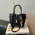 Elegante bolso de cubo negro con colgante de madera y herrajes plateados sobre libro - Negro