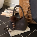 Sac seau rétro marron foncé avec pompon et pompon sur fond de livres anciens - Café avec Pendentif