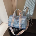 Blue denim cylinder tote bag with a wide floral embroidered shoulder strap in a mirror reflection - Light Blue