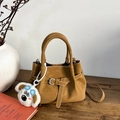Sac seau en daim marron avec coutures contrastées et breloque peluche sur un bureau en bois - Avec Pendentif / Marron