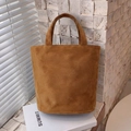 Dettaglio borsa tote in pelle scamosciata marrone con texture opaca su libro - Marrone