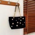 Black velvet tote bag with golden sunflower studs and chain strap shown on a wall hook - Black