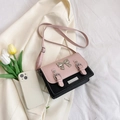 Bolso bandolera en rosa y negro con hebilla de lazo sobre fondo de traje beige - Rosa y Negro