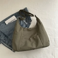 Bolso tote de nailon verde oliva con correa ajustable sobre fondo de tela blanca - Verde
