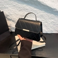 Quilted black crossbody bag with gold hardware and top handle shown on a display stand - Black