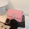 Pink leather square crossbody bag with silver oval buckle placed on a black book - Pink