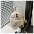 Detail view of corduroy backpack showing smiley face print and white pompom pendant - White