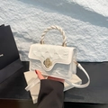 White crossbody bag with braided handle and gold clover clasp on a textured surface - White