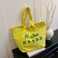 Bright yellow canvas tote bag with green Aloha print in a cozy minimalist home setting - Yellow