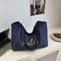 Borsa tote in denim retrò con ricamo Hello giallo e manici neri in un ambiente di caffè - Blu scuro